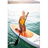 SUP Stand up paddle board concept - Pretty, young woman paddle boarding on a lovely lake in warm late afternoon light