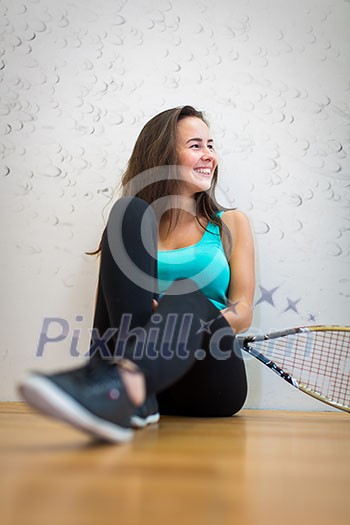 Cute young woman with a racket leaning against a wall in a squash court, ready for the game