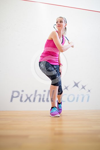 Cute young woman with a racket leaning against a wall in a squash court, ready for the game