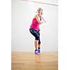 Cute young woman with a racket leaning against a wall in a squash court, ready for the game