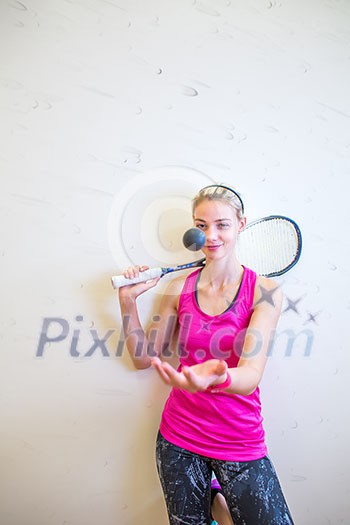 Cute young woman with a racket leaning against a wall in a squash court, ready for the game Cute young woman with a racket leaning against a wall in a squash court, ready for the game