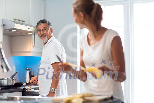Senior man cooking in a bright modern kitchen together with his daughter, having a blast (color toned image)