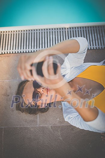 Young Beautiful Suntanned Woman wearing sunglasses relaxing next to a Swimming Pool  on a lovely Summer Day