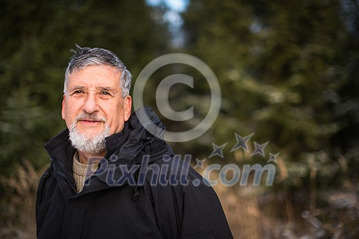 Portrait of a senior man, outdoor on a snowy forest path. Enjoying the crisp fresh air, watching the Sun go down.