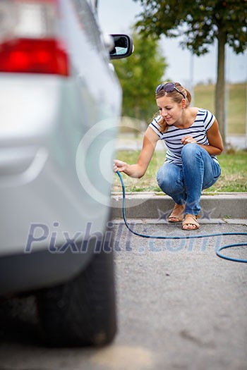 Young woman checking the car tyre pressure - inflating it