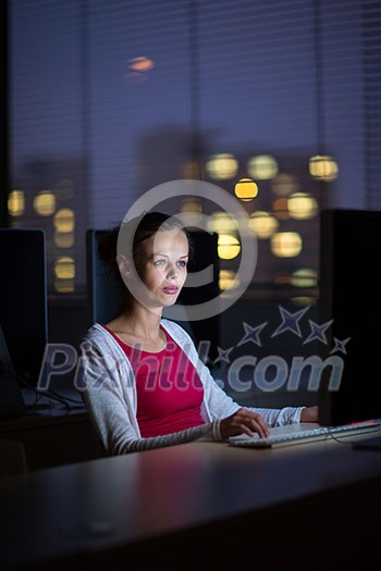 Pretty, young female college student using a desktop computer/pc in a college library - burning the midnight oil, working hard toward her goals instead of getting enough sleep (shallow DOF; color toned image)