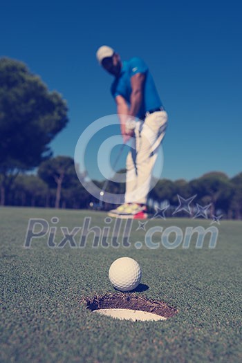 golf player hitting shot with driver, ball on edge of hole on course in background at beautiful sunny day golf player hitting shot with driver, ball on edge of hole on course in background at beautiful sunny day