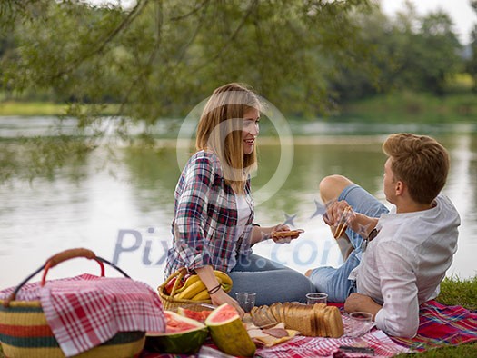 Couple in love enjoying picnic time drink and food in beautiful nature on the river bank Couple in love enjoying picnic time drink and food in beautiful nature on the river bank