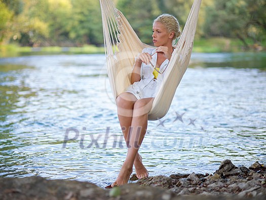 Young blonde woman resting on hammock while enjoying nature on the river bank Young blonde woman resting on hammock while enjoying nature on the river bank