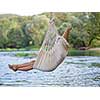 Young blonde woman resting on hammock while enjoying nature on the river bank