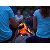 a group of happy young friends relaxing and enjoying  summer evening around campfire on the river bank