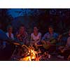 a group of happy young friends relaxing and enjoying  summer evening around campfire on the river bank