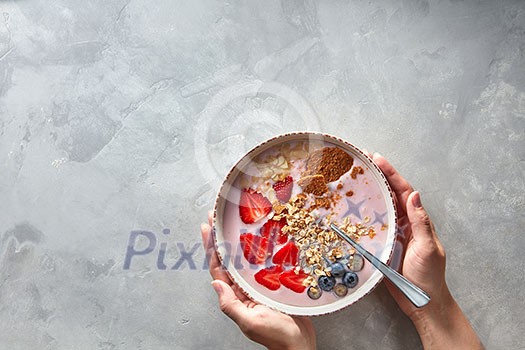 Light greek yogurt or cream dessert with almond flakes, oatmeal and fresh berry served in bowl in female hands on a concrete background, top view with space for text. Cleansing, diet, healthy food, fitness concept.