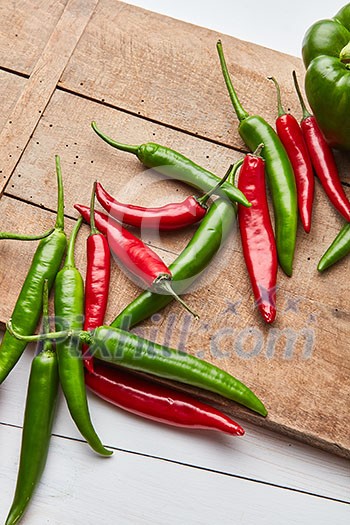 Colored green and red hot chili peppers on a wooden board with space under the text, top view