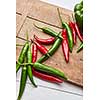 Colored green and red hot chili peppers on a wooden board with space under the text, top view