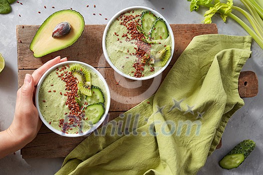 breakfast kiwi and cucumber smoothie bowl topped with avocado and flaxseeds in woman's hand on a cute wooden board with a green napkin, flat lay. Super Food