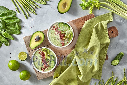Vegetable green smoothies with flax and kiwi in a plate on an old wooden board with a kitchen towel around a set of vegetables, avocado, cucumber, spinach, asparagus, lime, celery. Healthy Vegetarian Food. Flat lay Vegetable green smoothies with flax and kiwi in a plate on an old wooden board with a kitchen towel around a set of vegetables, avocado, cucumber, spinach, asparagus, lime, celery. Healthy Vegetarian Food. Flat lay