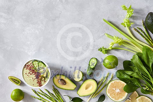 Vegetable collection, avocado, cucumber, spinach, asparagus, lime and plate with homemade fresh smoothies on a gray concrete background with copy space. Organic healthy food. Top view