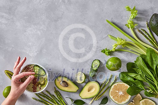 A woman's hand puts a plate of fresh asparagus asparagus. Angled frame of avocado, kiwi, cucumber, asparagus, lime on a gray concrete background with copy space. Top view