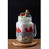 Healthy breakfast chia pudding with strawberries, banana and yogurt in glass mason jar on a dark wooden background