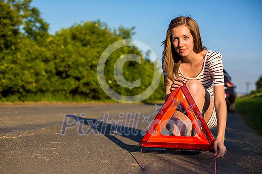 Pretty, young woman setting the safety triangle on the roadside after her car has broken down Pretty, young woman setting the safety triangle on the roadside after her car has broken down