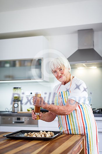 Senior woman cooking in the kitchen - eating and cooking healthy for her family; putting some potates in the oven, enjoying active retirement (shallow DOF; color toned image)