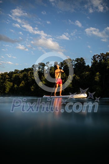 Handsome young man on a paddle board. Getting a great exercise on a lovely river in warm evening sunlight Handsome young man on a paddle board. Getting a great exercise on a lovely river in warm evening sunlight
