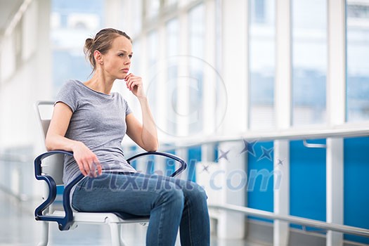 Female patient, sitting in a wheelchair for patients feeling not well enough to stand, waiting to be taken care of in a modern hospital (shallow DOF; color toned image)