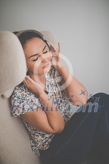 Pretty, young woman listening to her favorite music on hi-fi headphones sitting in a designer chair Pretty, young woman listening to her favorite music on hi-fi headphones sitting in a designer chair
