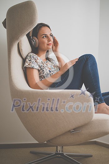 Pretty, young woman listening to her favorite music on hi-fi headphones sitting in a designer chair Pretty, young woman listening to her favorite music on hi-fi headphones sitting in a designer chair