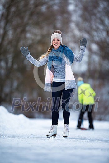 Young woman ice skating outdoors on a pond on a freezing winter day (color toned image; motion blurred image)