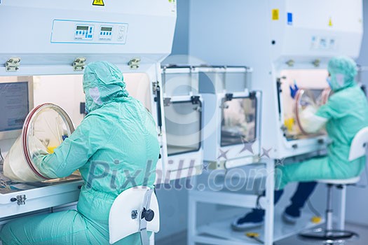 Pharmaceutical technician in sterile environment working on production of pills at pharmacy factory (shallow DOF; color toned image) Pharmaceutical technician in sterile environment working on production of pills at pharmacy factory (shallow DOF; color toned image)