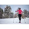 Cross-country skiing: young woman cross-country skiing on a winter day (forest in focus, skier left out of focus)