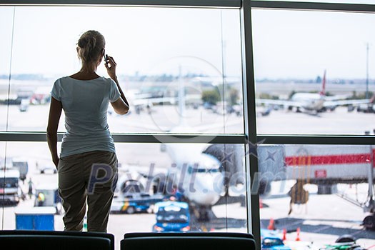 Pretty, young woman waiting at a gate area of a modern airport for  the boarding call - making some calls(color toned image; shallow DOF)