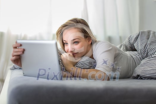 Pretty, young woman in her bed using her tablet computer, staying up to date with news and socail networks she likes(color toned image; shallow DOF)
