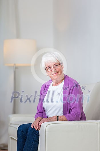 Portrait of a senior woman at home - Looking happy, looking at the camera, smiling while sitting on the sofa in her living room
