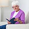 Portrait of a senior woman at home - Looking happy, looking at the camera, smiling while sitting on the sofa in her living room and reading a good book
