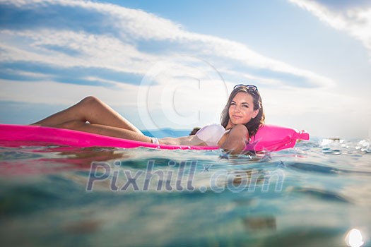 Pretty, young woman enjoying a day at the beach, relaxing on inflatable mattress