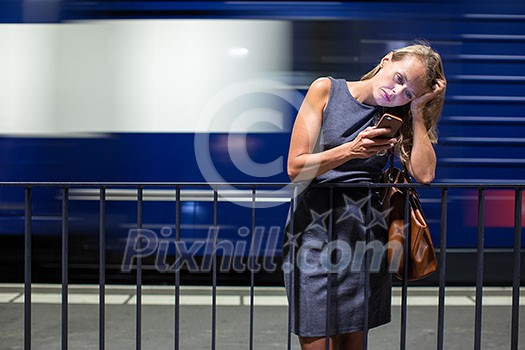 Pretty, young female commuter waiting for her daily train in a modern trainstation, using her cellphone while waiting (color toned image)