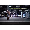 Pretty, young female commuter waiting for her daily train in a modern trainstation, using her cellphone while waiting (color toned image)