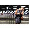 Pretty, young female commuter waiting for her daily train in a modern trainstation, using her cellphone while waiting (color toned image)