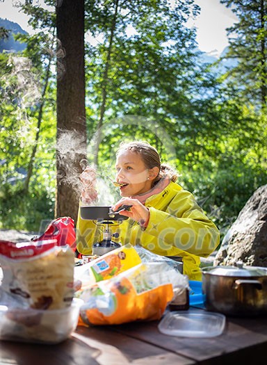 Female hiker/climber preparing supper on gas burner in a camp