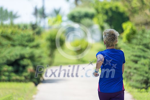 young sporty female runner training for marathon running at beautiful tropical park in the sunny morning