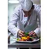 chef serving vegetable salad on plate in restaurant kitchen