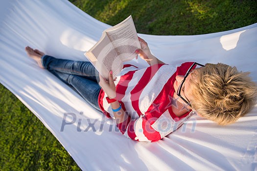 young woman reading a book while relaxing on hammock in a peaceful garden during holiday