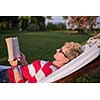 young woman reading a book while relaxing on hammock in a peaceful garden during holiday