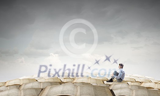 Young businessman sitting alone on pile of old books