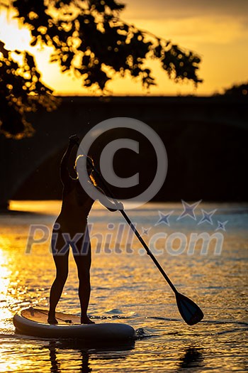 SUP Stand up paddle board concept - Pretty, young woman paddle boarding on a lovely lake in warm late afternoon light - shot from underwater