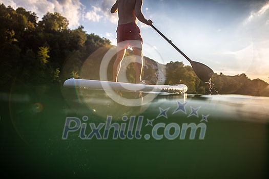 Handsome young man on a paddle board. Getting a great exercise on a lovely river in warm evening sunlight Handsome young man on a paddle board. Getting a great exercise on a lovely river in warm evening sunlight