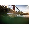 Handsome young man on a paddle board. Getting a great exercise on a lovely river in warm evening sunlight